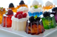 Colorful fruit jelly desserts topped with whipped cream and fresh berries on white serving plate, perfect for party catering.