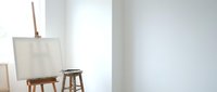 Minimalist art studio interior with blank canvas on wooden easel and stool against white walls creating peaceful creative workspace for painting.