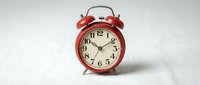 Vintage red twin bell alarm clock with white face and Arabic numerals on neutral background, suitable for time management, scheduling, and retro design projects.