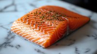 Fresh raw salmon fillet with herbs and spices on marble surface, showing vibrant orange color and marbled texture, ready for cooking preparation.