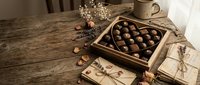 Luxury chocolate truffles in elegant gift box on rustic wooden table with coffee cup and decorative flowers for Valentine's Day or special occasion celebration.