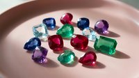 Collection of colorful precious gemstones including emerald, ruby, sapphire and amethyst arranged on pink ceramic plate for jewelry making and luxury design.