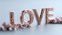Rose gold glittery letters spelling LOVE on white surface with soft focus decorative elements creating romantic atmosphere for wedding and valentines designs.