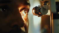 Close-up of African American male patient during eye examination with slit lamp biomicroscope in dark room, dramatic lighting highlights eye detail.
