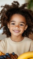 Happy mixed-race child with curly hair smiling at breakfast table with healthy fruits and cereal, promoting nutritious eating habits for kids.