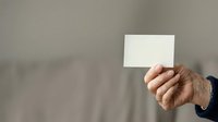 Hand holding blank white card against neutral gray background, suitable for business branding, marketing mockups, and corporate presentations.