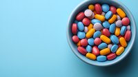 Colorful pharmaceutical pills and capsules in blue ceramic bowl on pastel blue background. Medical and healthcare concept with copy space.