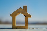Wooden house-shaped cutout silhouette against blurred blue background symbolizing real estate, property investment, and home ownership concept.