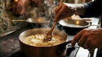 Hands stirring cooked rice in metal pot during meal preparation, traditional cooking method for food service and culinary education.
