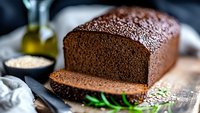 Fresh baked dark rye bread loaf with sliced piece on wooden cutting board, sprinkled with seeds and herbs, rustic food photography setup.