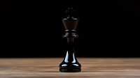 Black chess king piece standing alone on wooden surface against dark background, dramatic lighting highlights strategic game piece for business concepts.