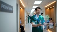 Male doctor in green scrubs using digital tablet with holographic interface in modern hospital corridor for healthcare technology applications.