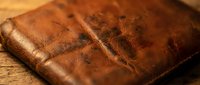 Vintage brown leather wallet with worn texture and stitched edges on rustic wooden surface for fashion and lifestyle concepts.