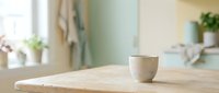 Wooden table with ceramic cup in bright, minimalist kitchen interior with natural light and blurred background, suitable for home decor and lifestyle design projects.