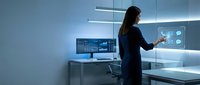 Woman in dark business suit analyzing digital data on multiple screens in modern tech workspace with blue lighting and holographic interface elements.