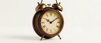 Vintage bronze twin bell alarm clock with Roman numerals on cream dial, standing on white background for home decor and time management concepts.