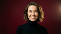 Professional businesswoman with short brown hair smiling confidently in black turtleneck against warm burgundy background for corporate headshots.