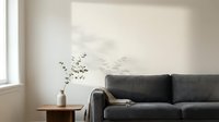 Dark gray upholstered sofa with wooden side table holding white vase with dried branches in minimalist living room with natural light from window.