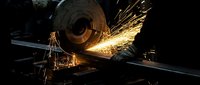 Industrial metalworking with angle grinder creating bright sparks in dark workshop environment for manufacturing and fabrication projects.