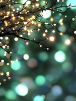 Glowing fairy lights on dark tree branches against blurred emerald green bokeh background create magical holiday atmosphere. For seasonal greeting cards and decor.