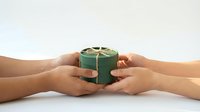 Hands exchanging green gift box with golden ribbon bow on white background for holiday celebration and special occasions.