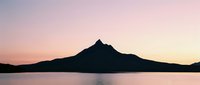 Mountain silhouette reflected in calm lake water at sunset, creating serene landscape scenery for nature and travel projects.