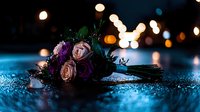 Wedding bouquet with pink and purple roses lying on wet surface with romantic bokeh lights in dark blue evening atmosphere creating dreamy mood.