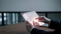 Businessman holding transparent futuristic tablet with glowing interface in modern office environment showcasing advanced technology and digital innovation.