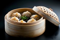 Steamed dumplings in traditional bamboo basket with soy sauce and fresh herbs on dark background, dramatic lighting highlights Asian cuisine delicacy.