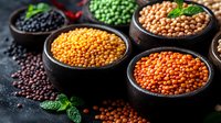 Colorful variety of raw lentils and legumes in black ceramic bowls on dark background with fresh mint leaves. Healthy protein source for vegetarian cuisine.