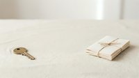 Vintage brass key and tied envelope on neutral linen fabric surface, minimalist flat lay composition for design, stationery, and correspondence themes.