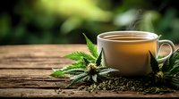Hot steaming cup of herbal cannabis tea with fresh marijuana leaves on rustic wooden table, therapeutic natural medicine concept with copy space.