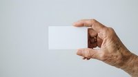Mature male hand holding blank white business card against neutral background for corporate branding and marketing purposes.