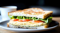 Fresh sandwich with crispy toasted bread, layered with lettuce, juicy tomato slices and tuna salad filling on gray ceramic plate, selective focus on dark background.