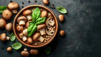 Fresh brown champignon mushrooms in rustic ceramic bowl with basil leaves on dark stone background, raw organic food ingredients for cooking.