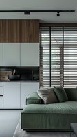 Modern minimalist studio apartment interior with green sofa, white kitchen cabinets, wooden accents, and large window with horizontal blinds. Clean lines and monochromatic design.