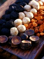 Assorted dried fruits and nuts arranged in diagonal rows on dark wooden board, including black prunes, white walnuts, and dried apricots in warm lighting.