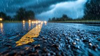 Dramatic wet asphalt road with yellow line markings reflecting street lights during heavy rain storm at dusk, low angle perspective creates moody atmosphere.