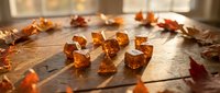 Amber gemstones scattered on rustic wooden surface with autumn leaves in warm sunlight for jewelry design and crafting projects.