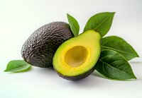 Fresh ripe avocado cut in half showing pit and creamy yellow flesh with whole dark avocado and green leaves on white background for healthy eating concept.