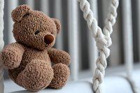 Soft brown teddy bear sitting near white braided rope on blurred background. Close up view of plush toy with selective focus creates cozy nursery atmosphere.