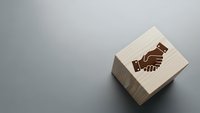 Wooden rubber stamp with handshake symbol on gray surface for business partnership and agreement concepts in corporate branding applications.