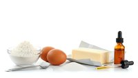 Fresh eggs, butter, flour and vanilla extract arranged for baking preparation on clean white background, isolated ingredients ready for cooking projects.