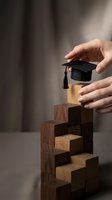 Hands placing graduation cap on wooden blocks staircase representing educational achievement and academic success journey.