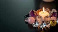 Hands holding burning candle surrounded by colorful healing crystals and gemstones for meditation, spiritual wellness and energy healing practices.