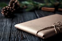 Elegant rose gold gift wrapped with rustic twine on dark wooden background with pine cone and winter decorations, creating cozy holiday atmosphere.