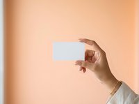 Hand holding blank white card against warm beige background, suitable for business card mockups, promotional materials, and branding presentations.