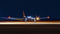 Private jet on runway at night with dramatic lighting effects and glowing navigation lights against dark blue sky, ready for takeoff or after landing.