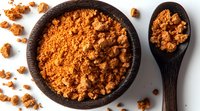 Ground palm sugar in black stone bowl and wooden spoon on white background, raw organic sweetener with caramel notes, traditional Asian ingredient.