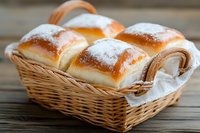 Fresh sweet buns with powdered sugar served in wicker basket on rustic wooden table, close up view of homemade pastries for breakfast or dessert.